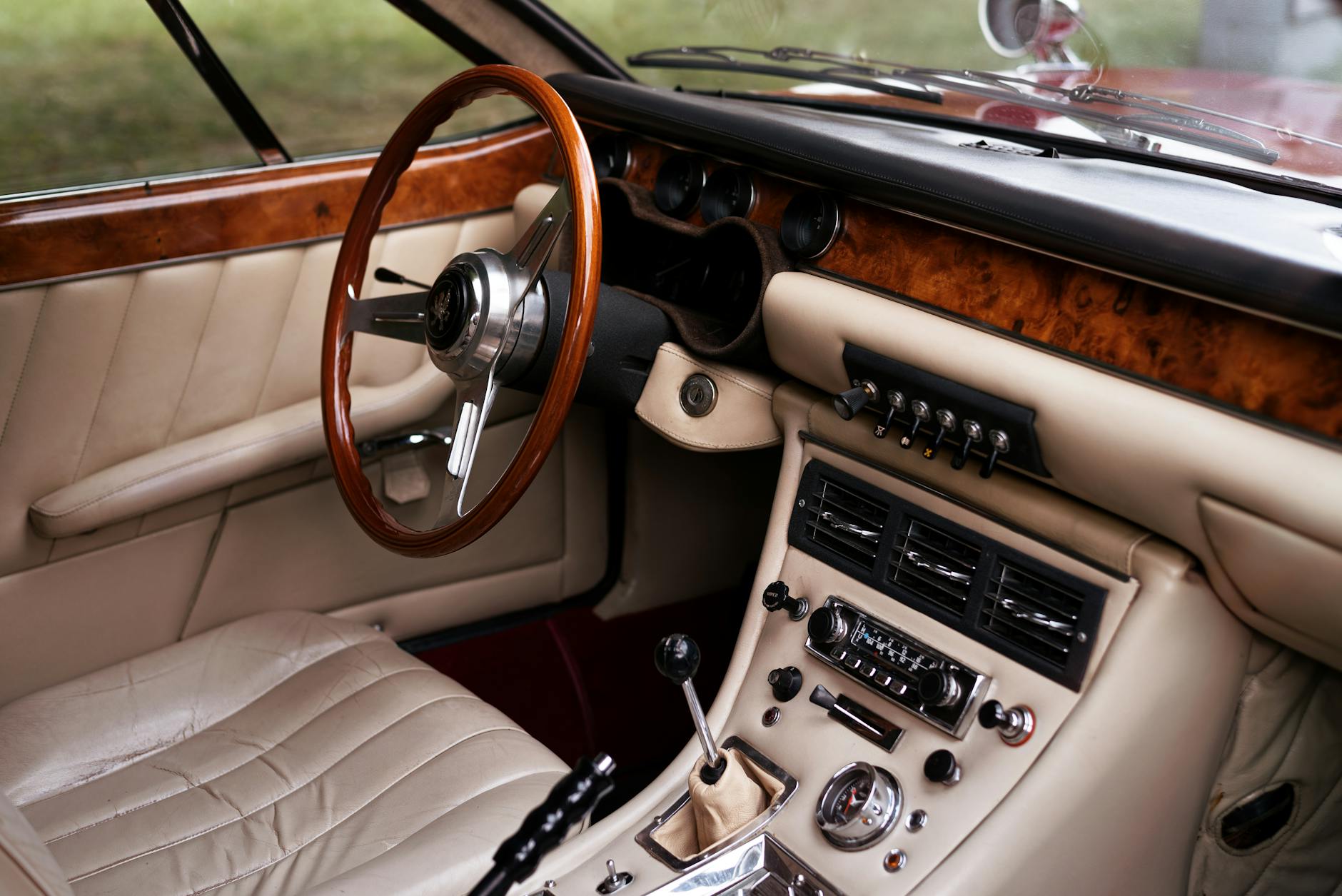Close-up of a vintage car interior featuring wooden trim, leather upholstery, and a classic dashboard.